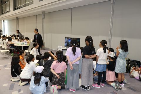 2024年に開催時の様子 MFPA説明のビデオを見ている子供たち　奥では口で描く体験も